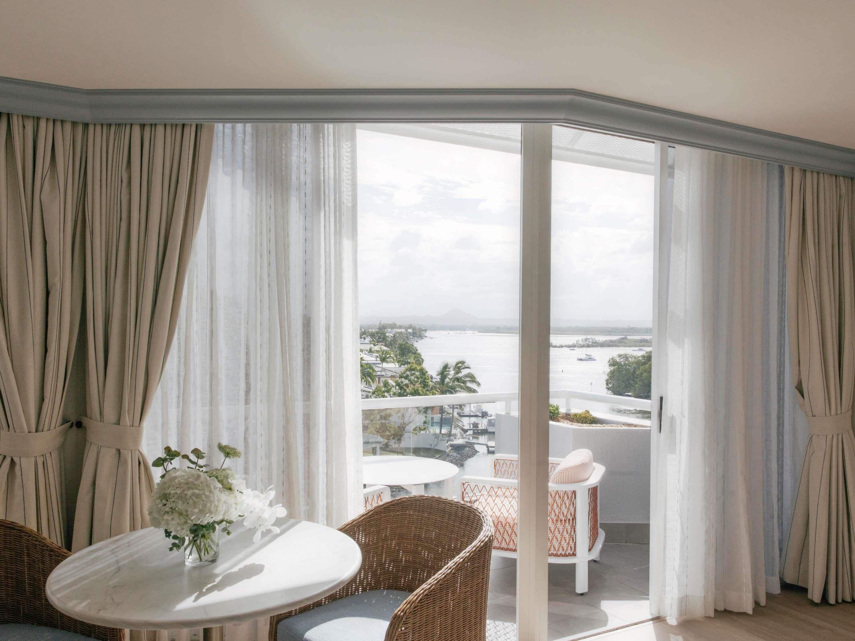 A balcony with a view of a body of water and distant landscape, furnished with wicker chairs and a table.