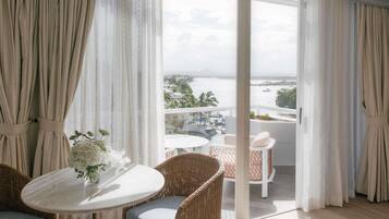 A balcony with a view of a body of water and distant landscape, furnished with wicker chairs and a table.