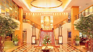 Eine großzügige Lobby mit einem geometrisch gemusterten Boden, einer zentralen Treppe und Blumentöpfen.