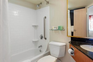 Ein Badezimmer mit Toilette, Waschbecken, Spiegel und einer Dusche mit Haltegriff.