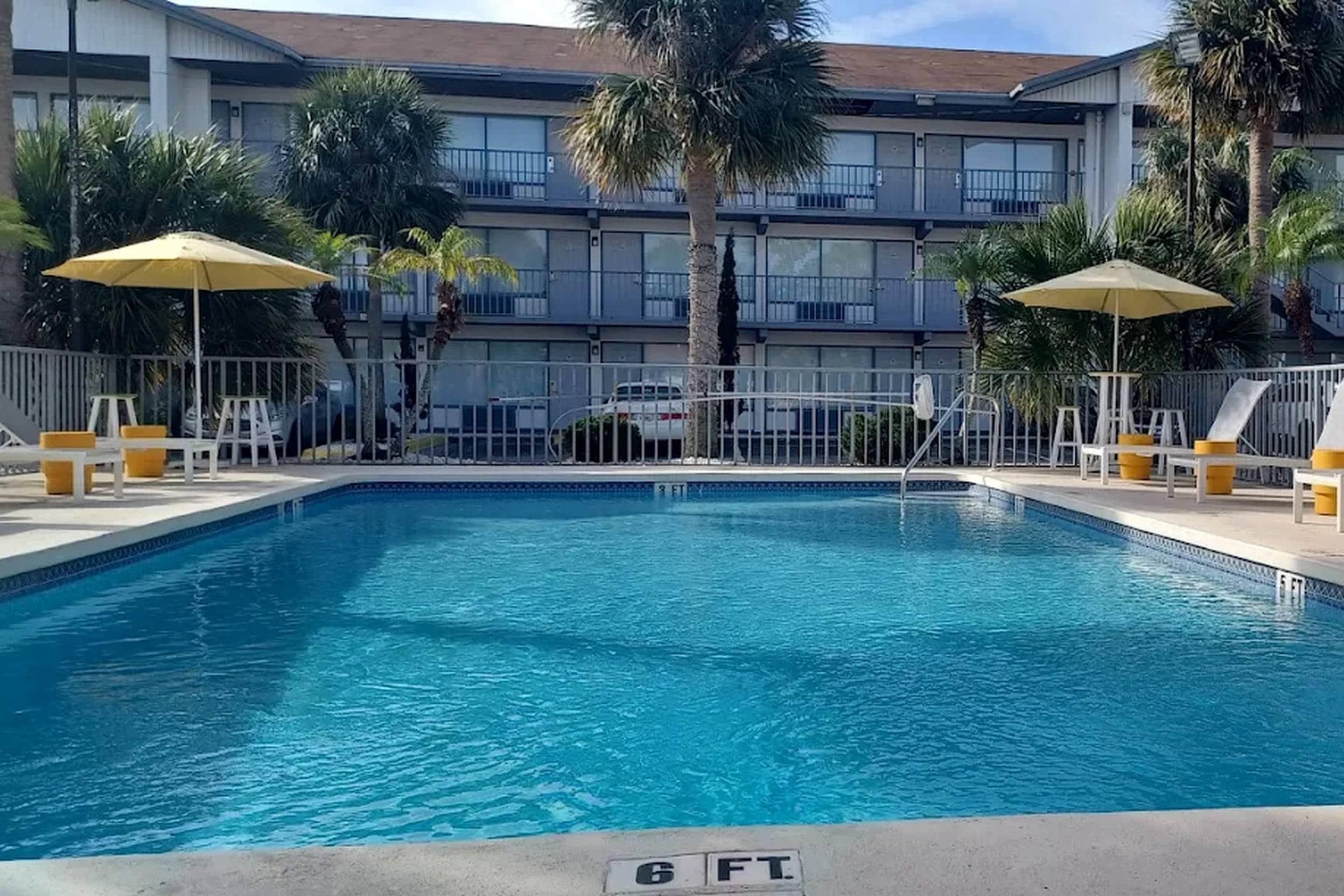 A swimming pool with a 6 FT depth marker, surrounded by a fence, with palm trees and umbrellas.