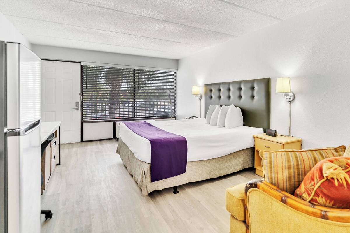 A hotel room with a bed, bedside lamps, a nightstand, a chair, and a window with blinds.