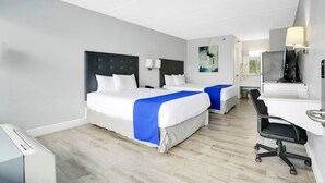 Ein Hotelzimmer mit zwei Betten, einem Schreibtisch, einem Stuhl, einem Fernseher und einem sichtbaren Badezimmer im Hintergrund.