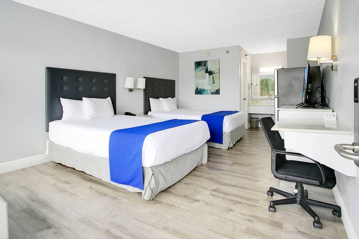 A hotel room with two beds, a desk, a chair, a TV, and a bathroom visible in the background.