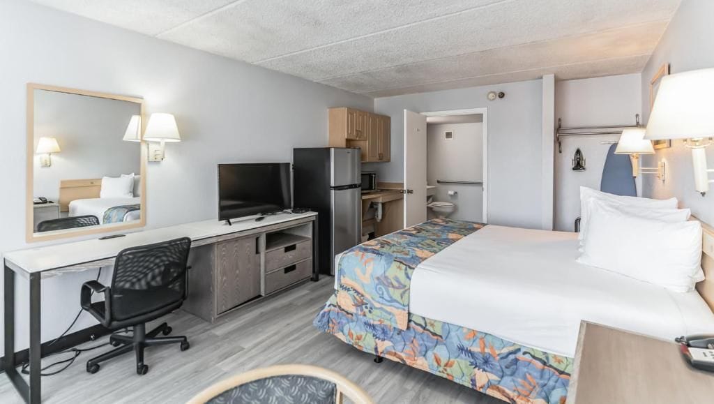 A hotel room with a bed, desk, chair, television, refrigerator, and a bathroom.
