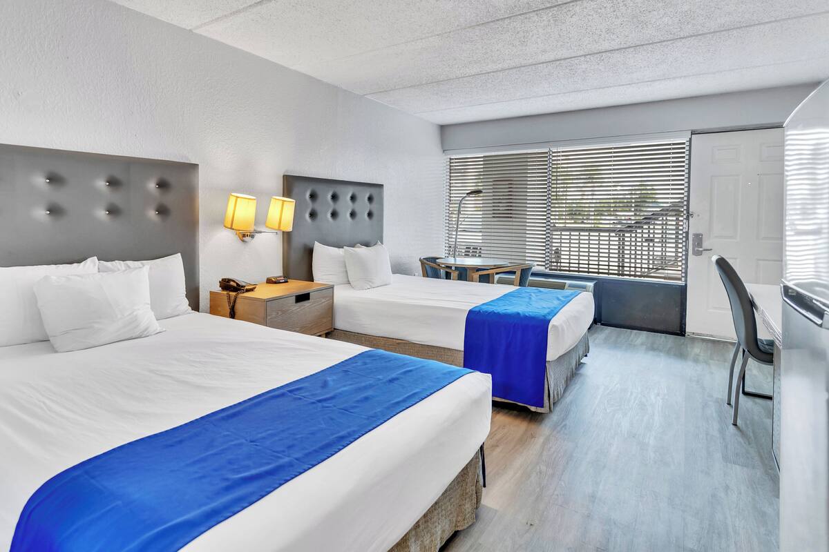 A hotel room with two beds, a desk, and a chair.