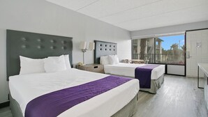 Ein Hotelzimmer mit zwei Betten, einem großen Fenster und einer Tür, die auf einen Balkon führt.