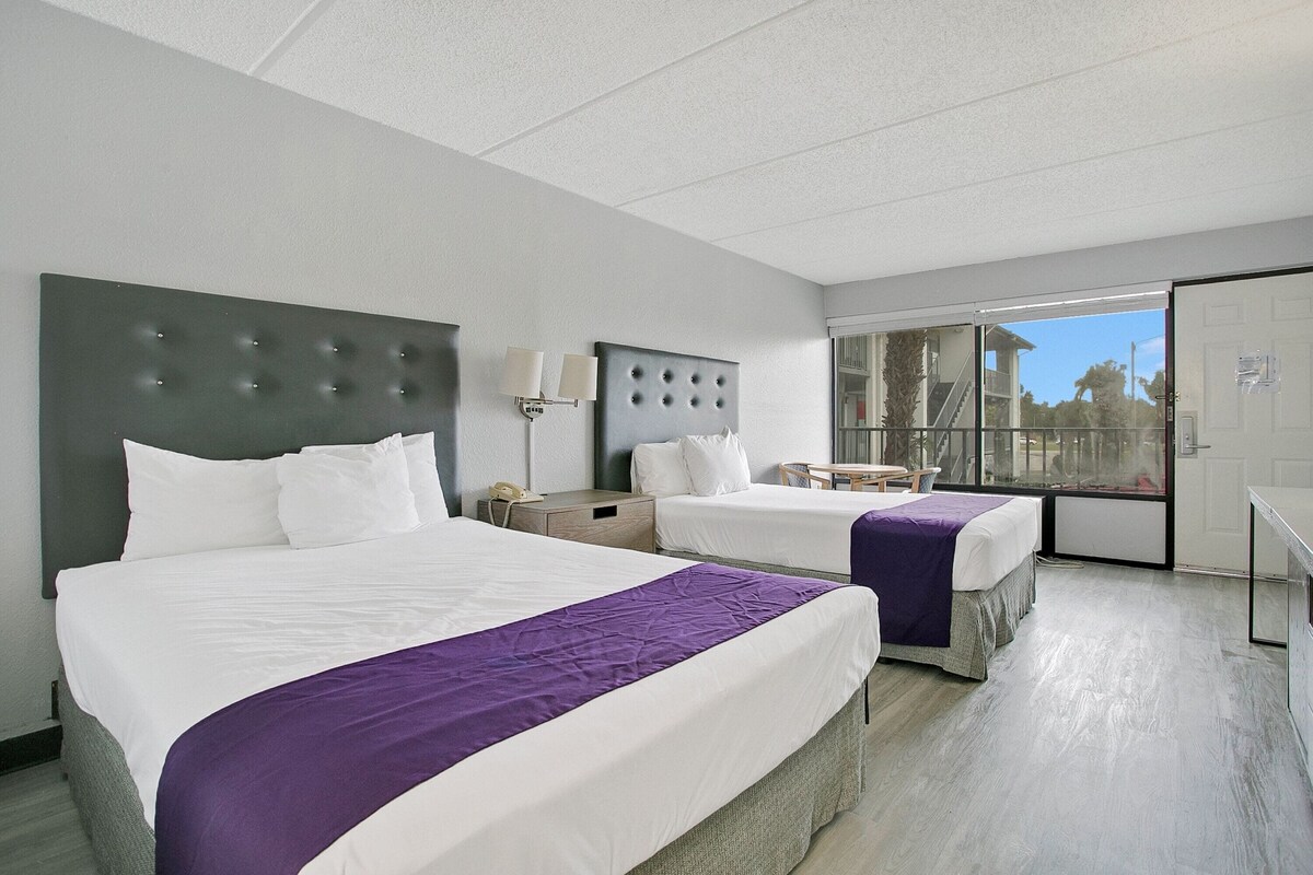 A hotel room with two beds, a large window, and a door leading to a balcony.