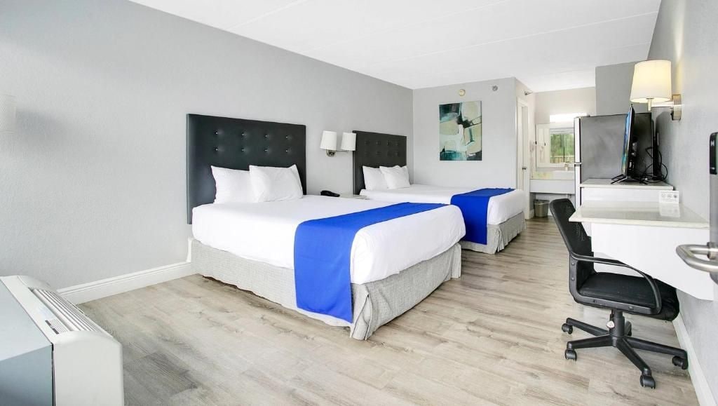 A hotel room with two beds, a desk, a chair, and a television.