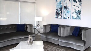 Ein modernes Wohnzimmer mit zwei grauen Sofas, einem Glastisch und abstrakter Wandkunst.