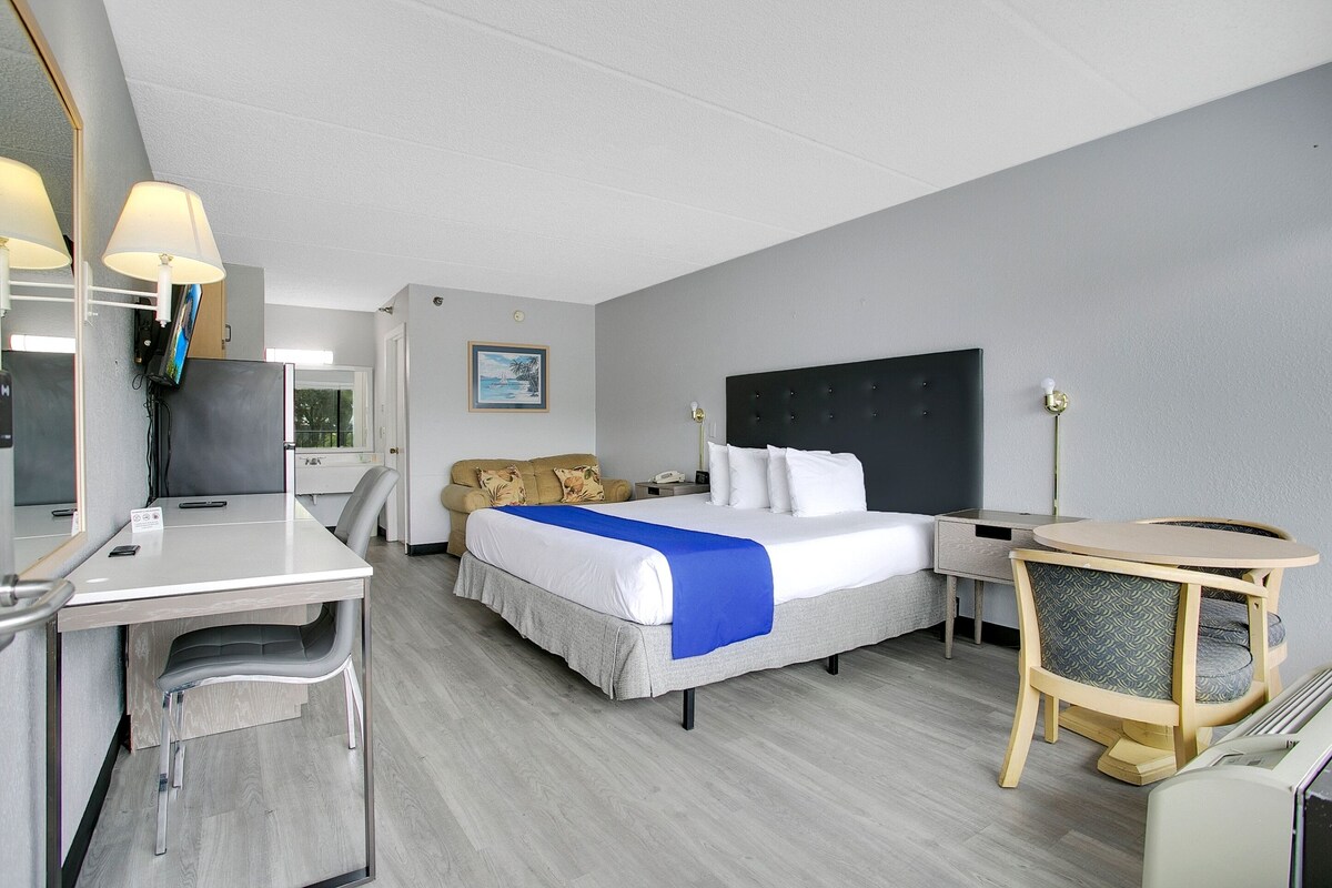 A hotel room with a bed, desk, chair, and a small round table with a chair.