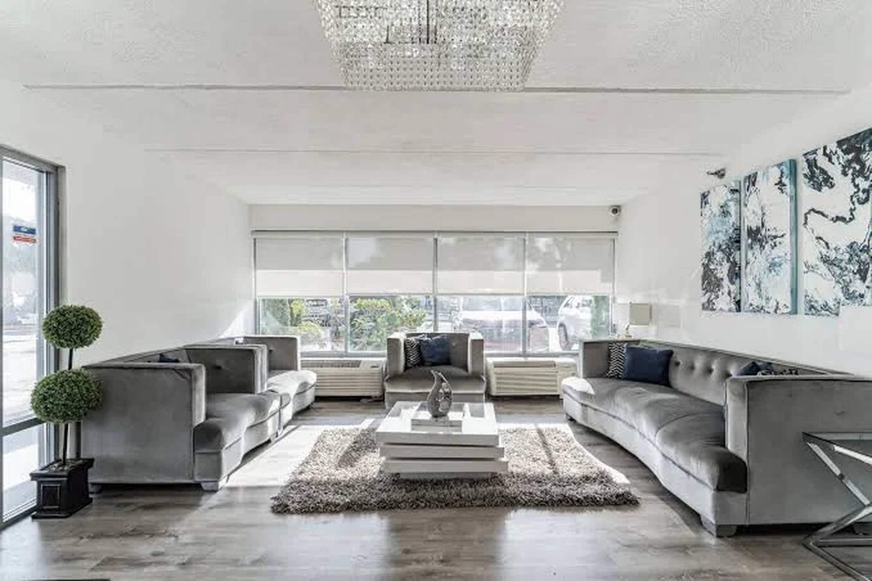 A modern living room with a chandelier, grey sofas, a coffee table, and a large window with a view.