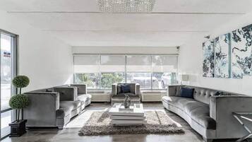 A modern living room with a chandelier, grey sofas, a coffee table, and a large window with a view.
