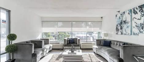 A modern living room with a chandelier, grey sofas, a coffee table, and a large window with a view.