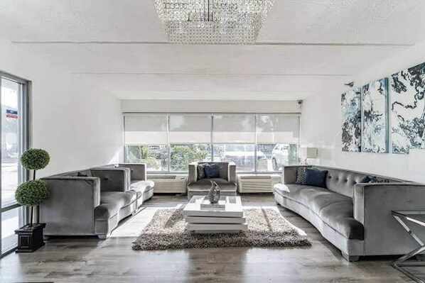 Un salon moderne avec un lustre, des canapés gris, une table basse et une grande fenêtre donnant sur un beau paysage.
