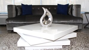 A modern living room with a sleek black sofa, two blue pillows, and a metallic vase on a white coffee table. - Home 1 Suites Extended Stay - Kissimmee (Kissimmee)