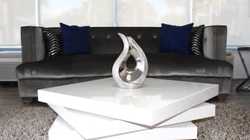 A modern living room with a sleek black sofa, two blue pillows, and a metallic vase on a white coffee table.