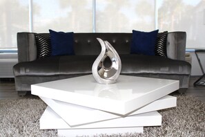 A modern living room with a sleek black sofa, two blue pillows, and a metallic vase on a white coffee table. - Home 1 Suites Extended Stay - Kissimmee (Kissimmee)