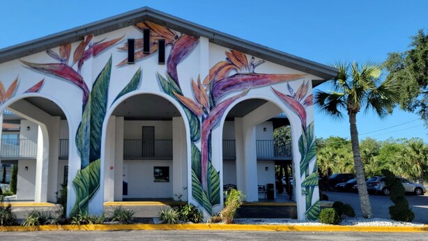 A building with a mural of tropical flowers on the facade, featuring three arched entrances and a balcony. - Home 1 Suites Extended Stay - Kissimmee (Kissimmee)