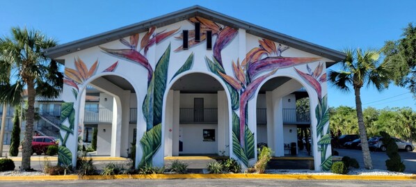 A building with a mural of tropical flowers on the facade, featuring three arched entrances and a balcony. - Home 1 Suites Extended Stay - Kissimmee (Kissimmee)