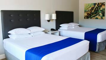 A hotel room with two beds, each with white bedding and a blue accent. There are two bedside tables with lamps, and a painting on the wall.