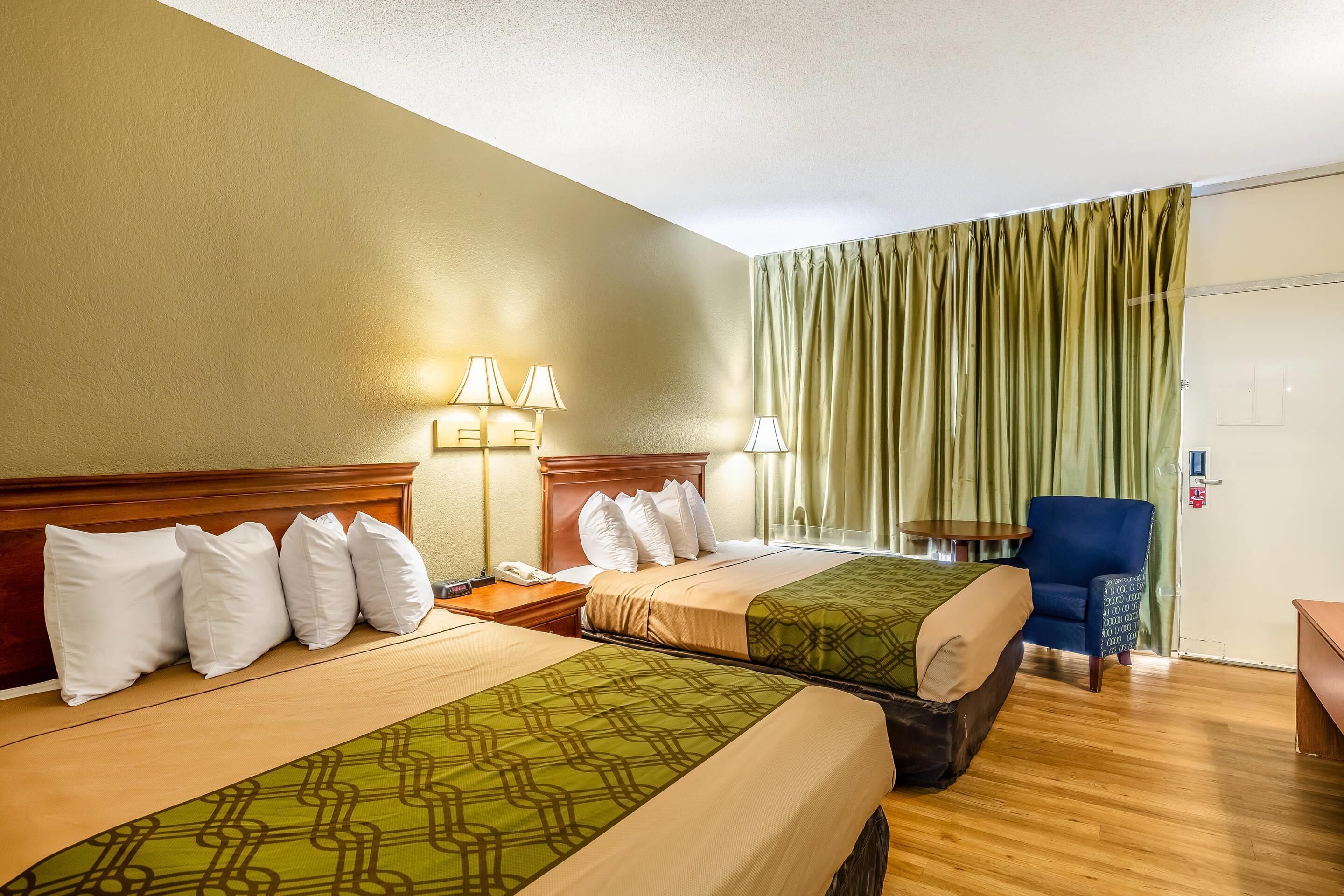 Quarto de hotel com duas camas, uma escrivaninha, uma cadeira e uma janela com cortinas.