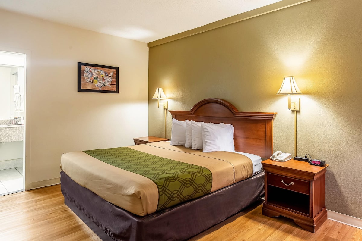 A hotel room with a bed, two bedside lamps, a nightstand with a phone, and a painting on the wall.