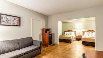 Quarto de hotel com sofá, micro-ondas, frigorífico e duas camas com abajures.