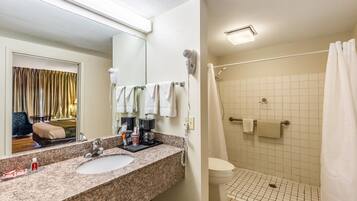 Une salle de bain d’hôtel équipée d’un lavabo, d’un miroir, d’un sèche-cheveux et d’une douche.