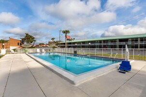 A swimming pool with a fenced area, a building with a green roof, and a flag.