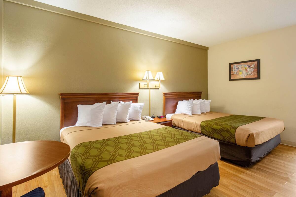 A hotel room with two beds, a round table, a lamp, and a wall map.