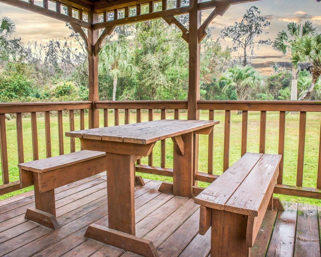 Eine Holzterrasse mit Picknicktisch und Bänken, umgeben von einem Holzgeländer.