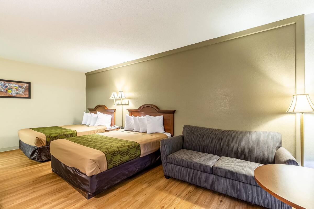 A hotel room with two beds, a sofa, a small table, and a lamp.