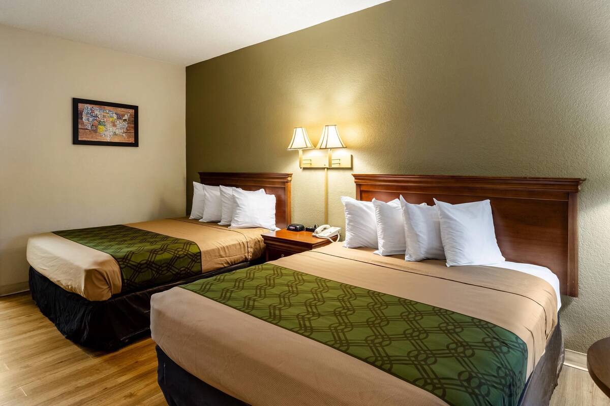 A hotel room with two beds, a nightstand, a lamp, and a framed map on the wall.