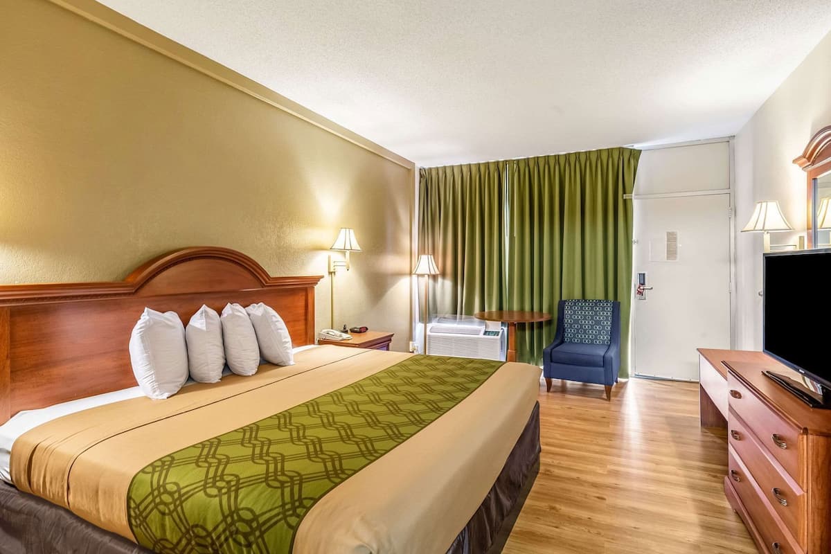 A hotel room with a bed, a chair, a TV, and a desk.