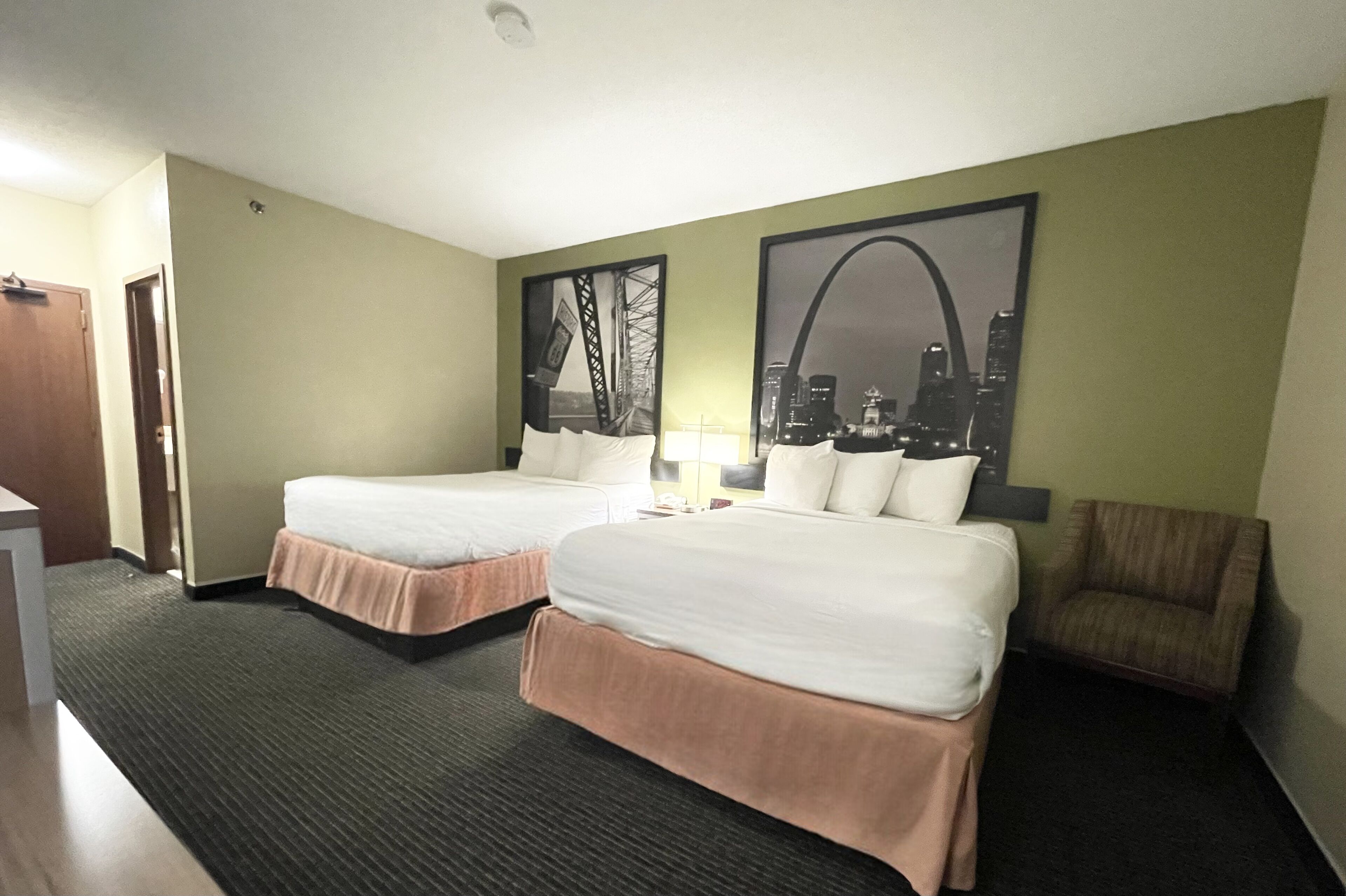 A hotel room with two beds, a chair, a desk, and two framed pictures on the wall.