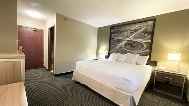 Ein Hotelzimmer mit einem großen Bett, zwei Nachttischen mit Lampen, einem Schreibtisch mit Stuhl, einer Tür und einer Wand mit einer Straßenkarte als Wandmalerei.