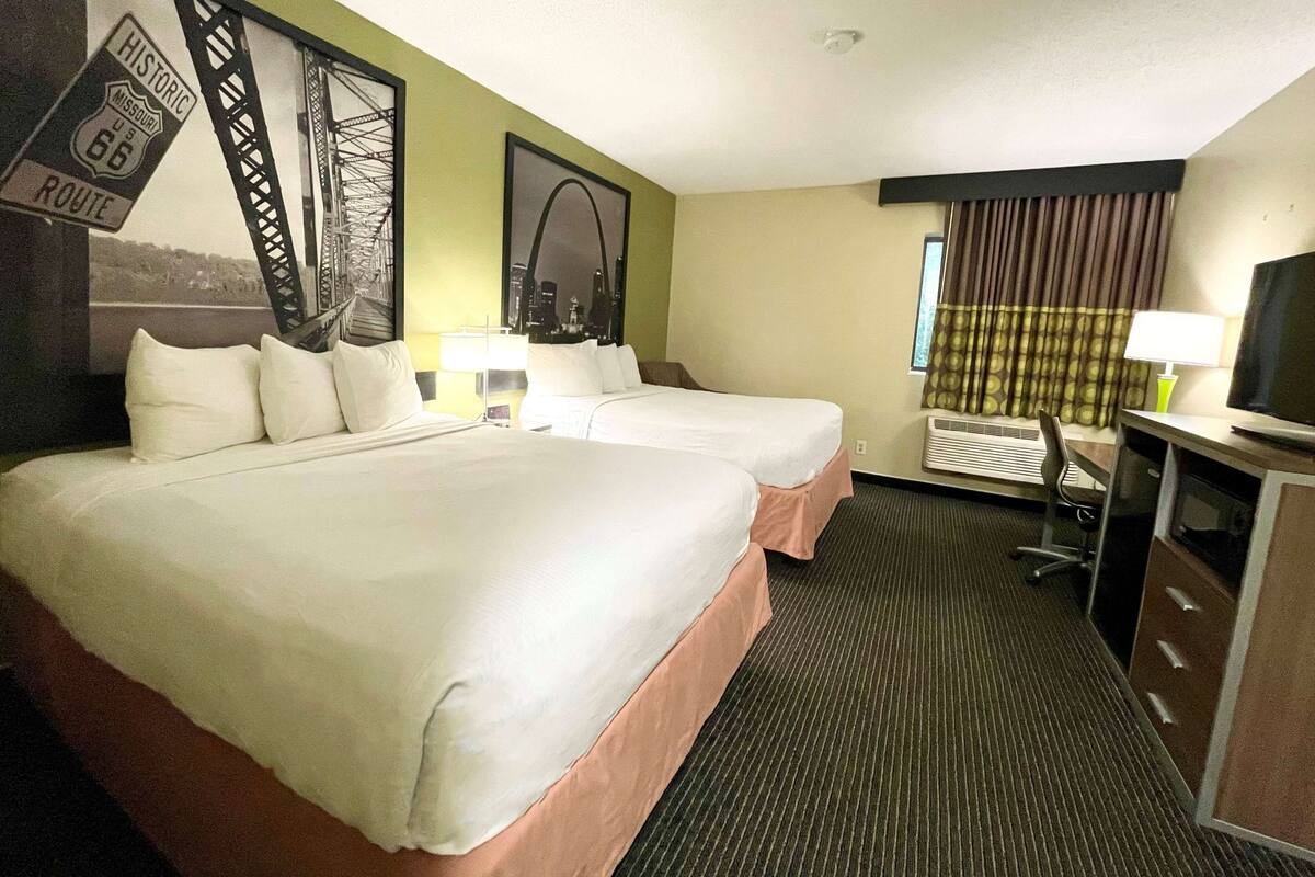 A hotel room with two beds, a desk, a chair, a TV, and a window with curtains.
