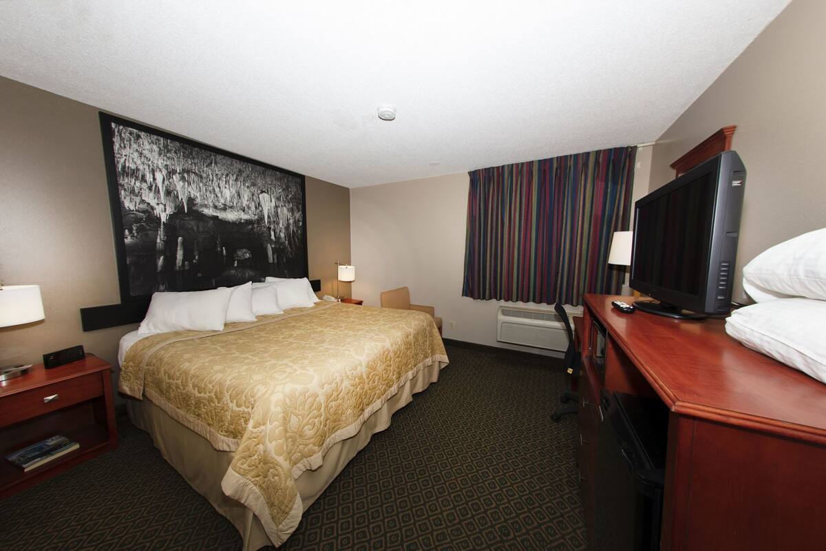 A hotel room with a large bed, a television, a desk with a lamp, and a large abstract painting on the wall.