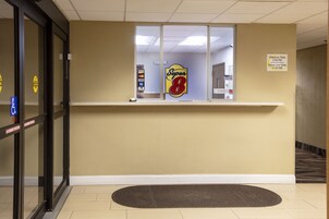 Un área de recepción con un letrero de Super 8, un cartel con los horarios de registro de entrada y salida, y un aviso sobre la política de mascotas.