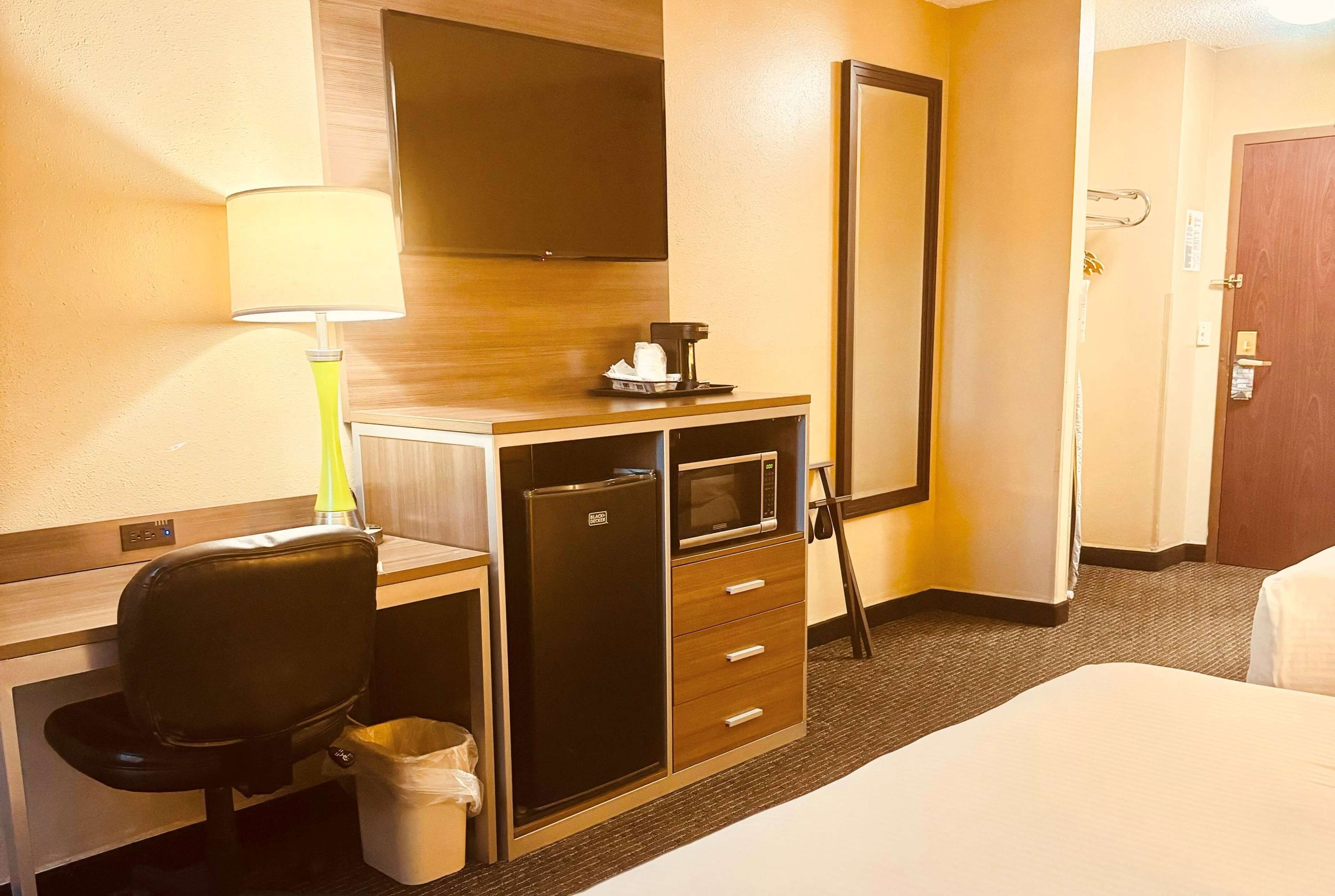 Habitación de hotel con cama, escritorio con silla, minibar, espejo y lámpara.