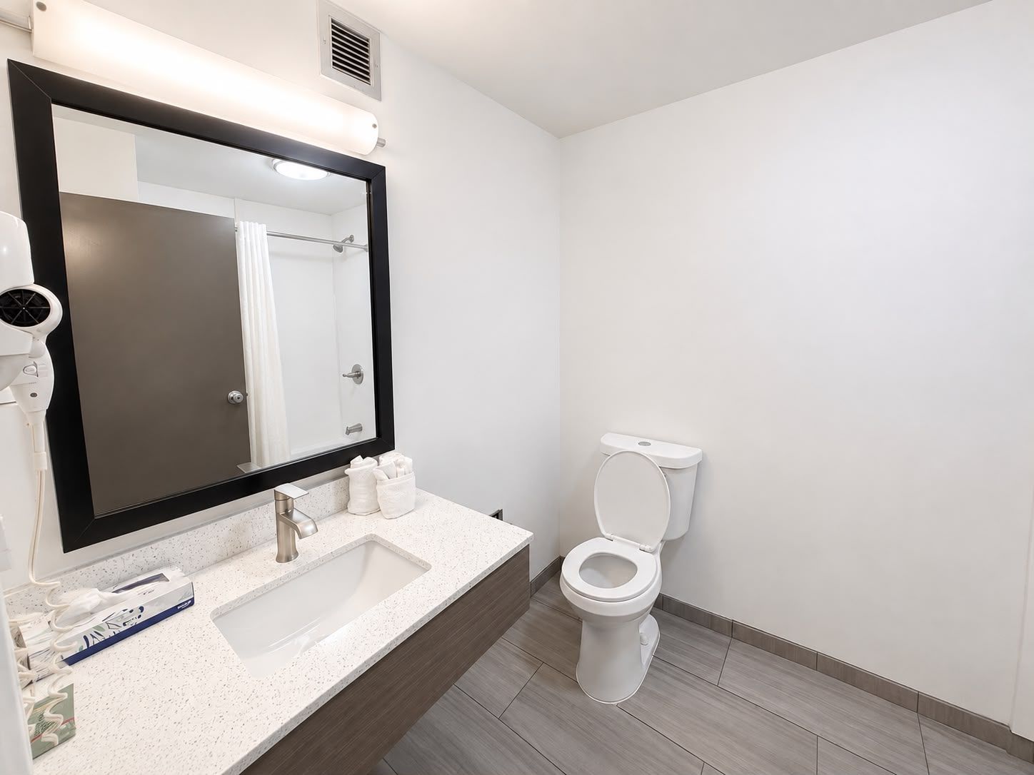 A modern bathroom with a large mirror, a white sink, and a toilet.