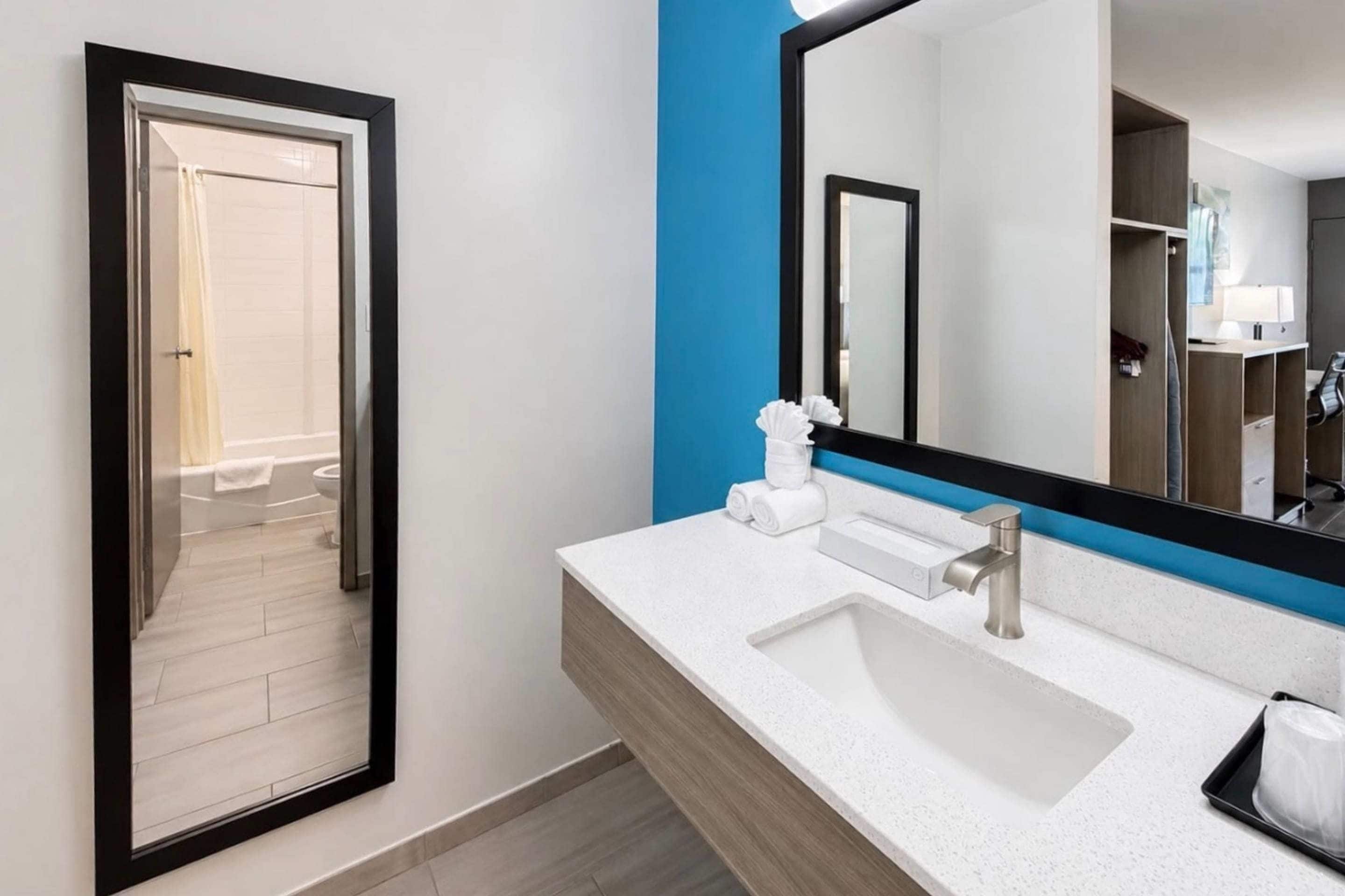A modern bathroom with a white sink, a large mirror, and a blue accent wall.