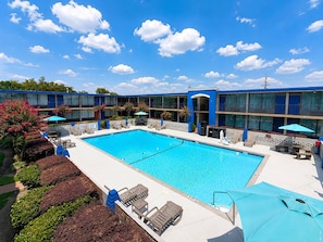 A hotel pool area with a clear blue sky, lounge chairs, and a building with blue accents. - Clarion Inn (Greenville)