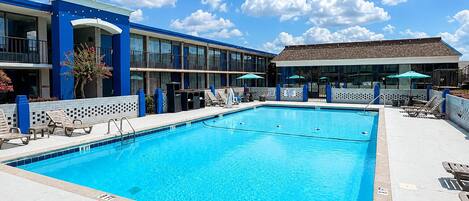 A swimming pool with lounge chairs, a building with blue and white exterior, and a clear blue sky.