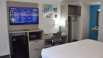 Une chambre d’hôtel équipée d’un lit, d’un bureau avec un ordinateur, d’un téléviseur affichant une liste des chaînes, d’un petit réfrigérateur et d’une étagère fixée au mur.
