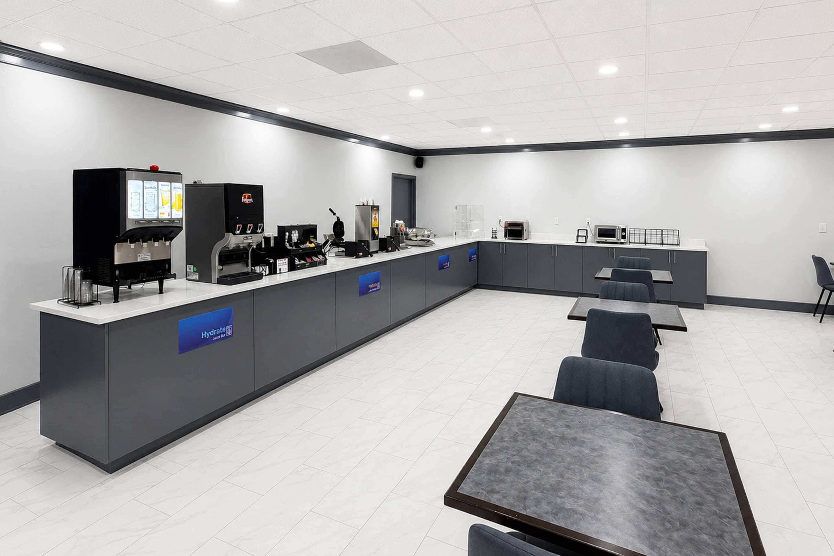 Uma sala de conferências moderna com uma mesa comprida, várias cadeiras, um canto para café e uma pequena cozinha.