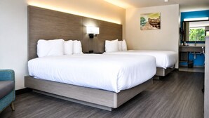 Une chambre d’hôtel avec deux lits, un bureau, une chaise, une lampe fixée au mur et un tableau.