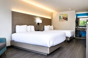 Habitación de hotel con dos camas, un escritorio, una silla, una lámpara de pared y un cuadro.