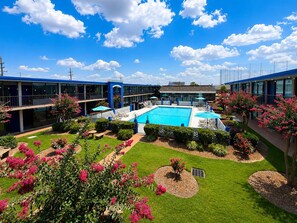 Ein Hotel mit Schwimmbad, umgeben von gepflegten Gärten und blauem Himmel.